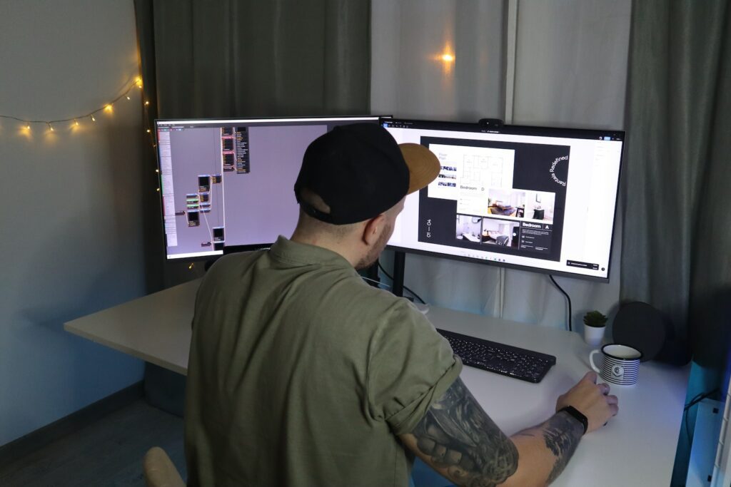 man in green dress shirt and black cap sitting in front of computer